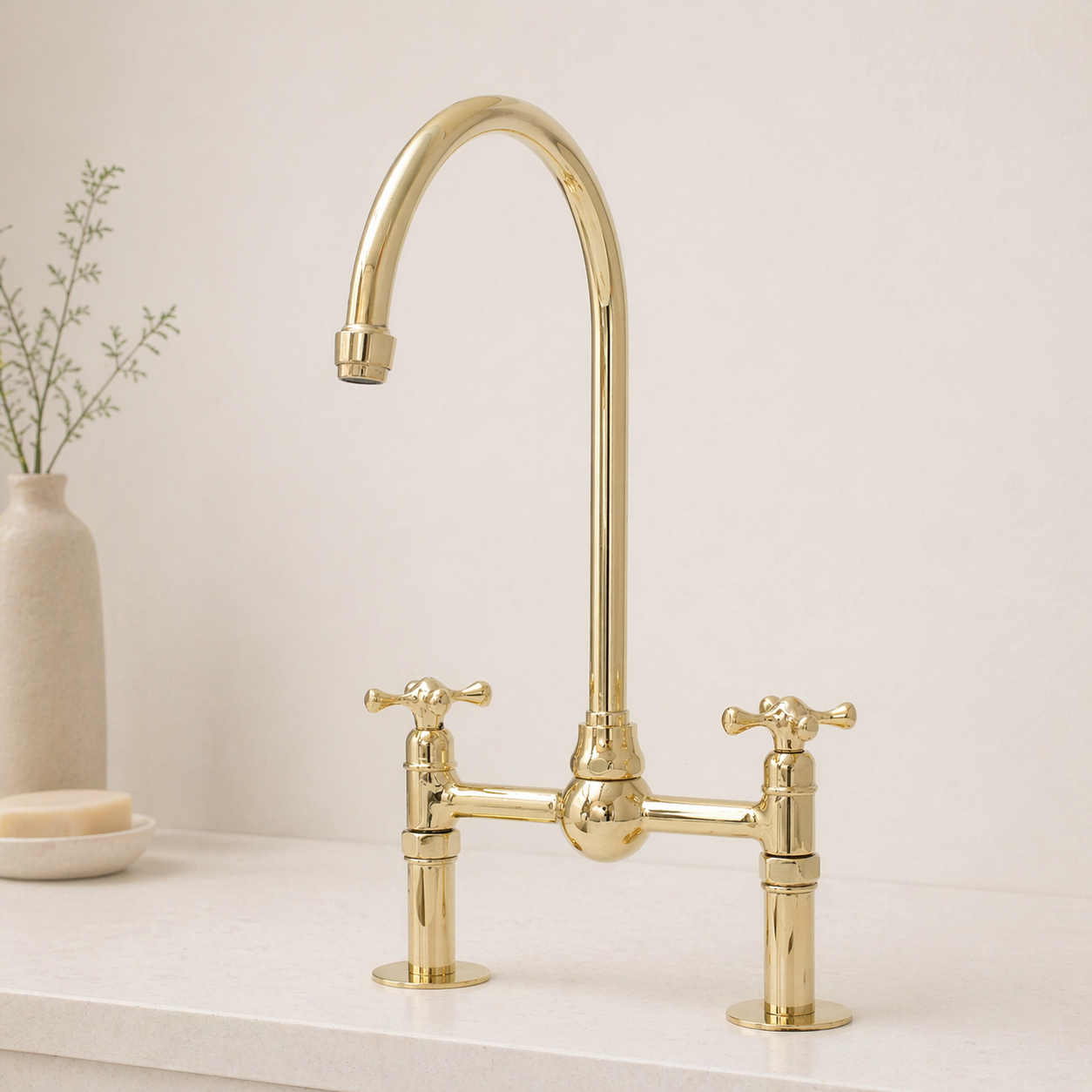 Angled view of polished unlacquered brass bridge faucet with curved spout and cross handles