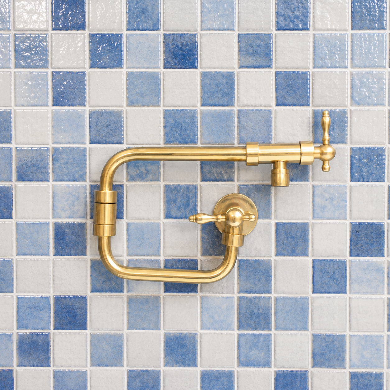 Handcrafted unlacquered solid brass wall mounted pot filler kitchen faucet with dual lever handles installed against blue tile backsplash