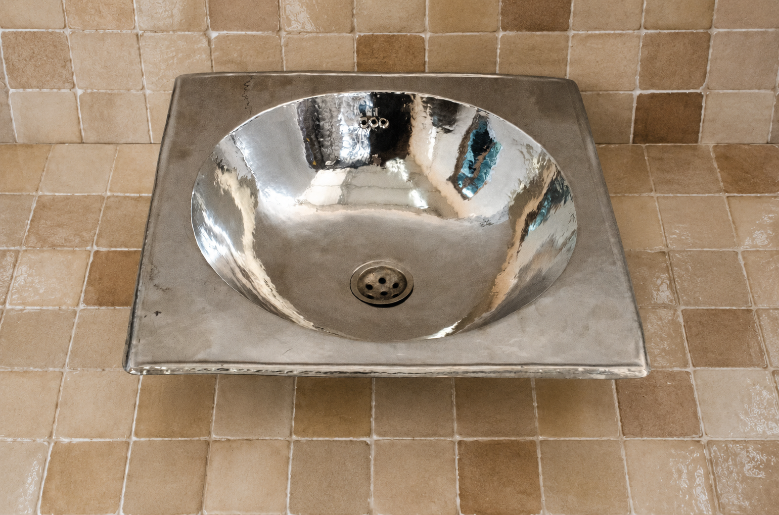Handcrafted German silver round vessel sink with hammered polished basin and square surround in a Moroccan tiled bathroom