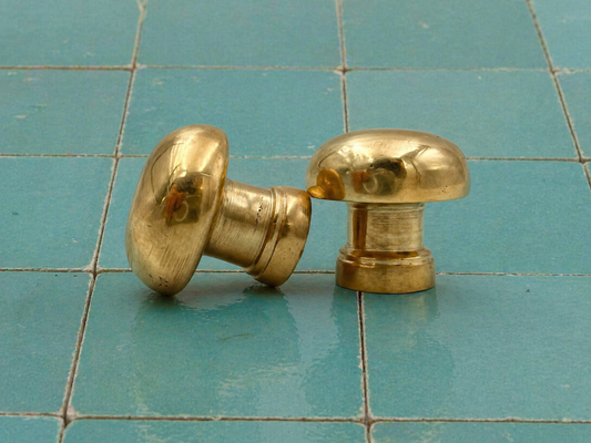 Handmade round unlacquered brass cabinet knobs displayed on blue Moroccan zellige tiles