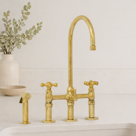 Moroccan handmade brass bridge kitchen faucet with cross handles and matching side sprayer installed on a white kitchen sink